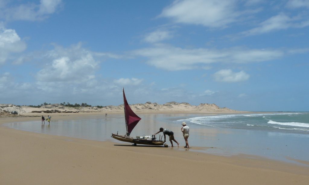 Two men pushing a jangada back up the beach. 