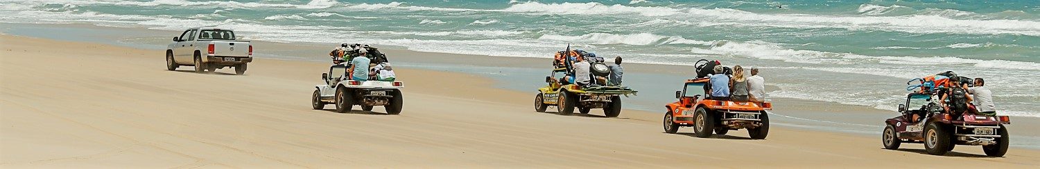 Panoramic shot of a convoy of buggies driving along the beach.